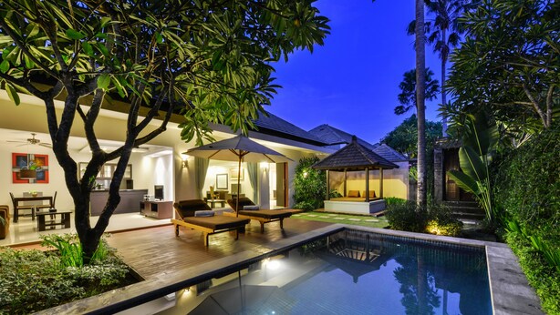 A modern outdoor pool area with lounge chairs and a covered seating area, surrounded by lush greenery and a well-maintained garden. - The Yubi Boutique Villas Seminyak (Seminyak)
