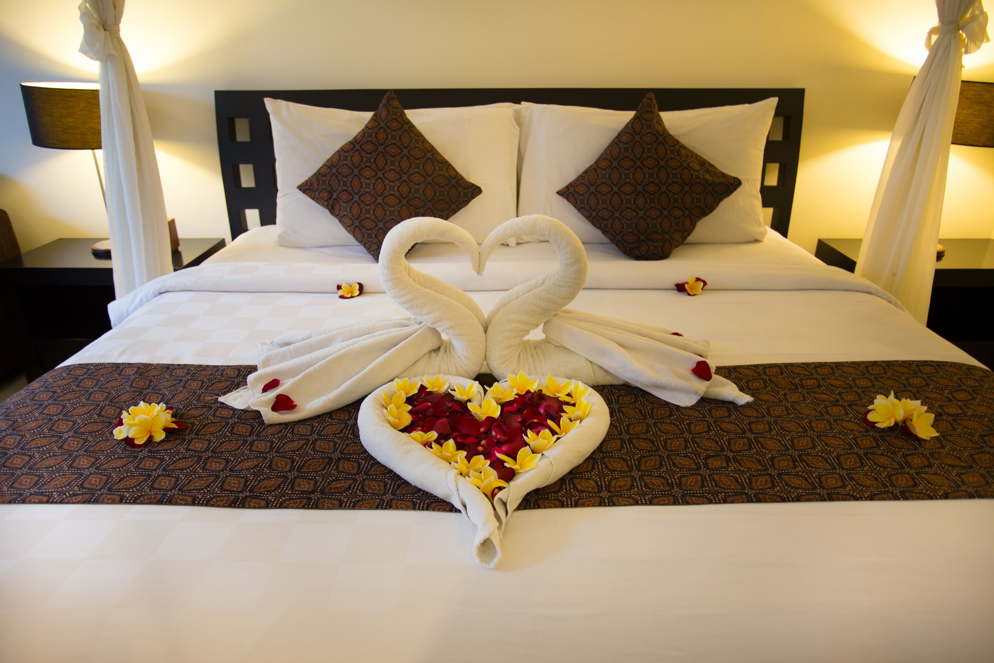A bed with a heart-shaped towel arrangement and rose petals.