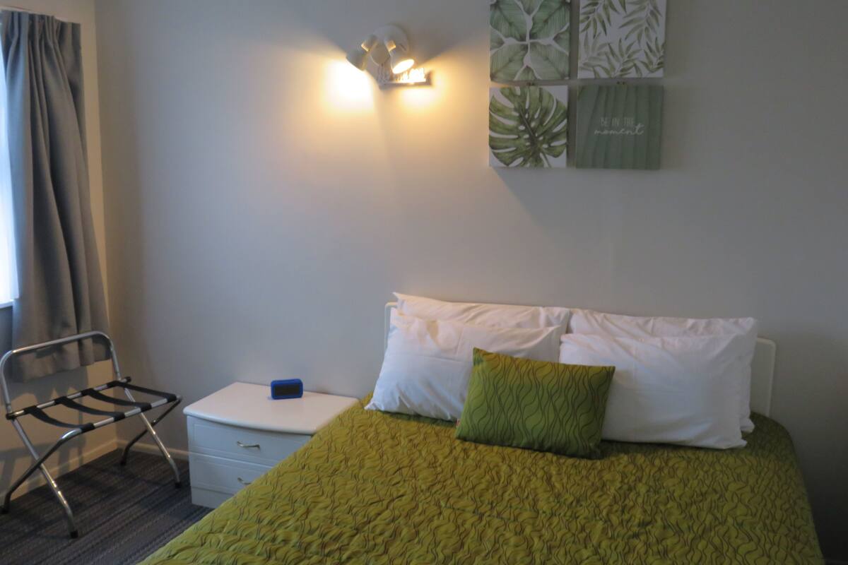 A bedroom with a bed, a bedside table, a chair, and wall art.