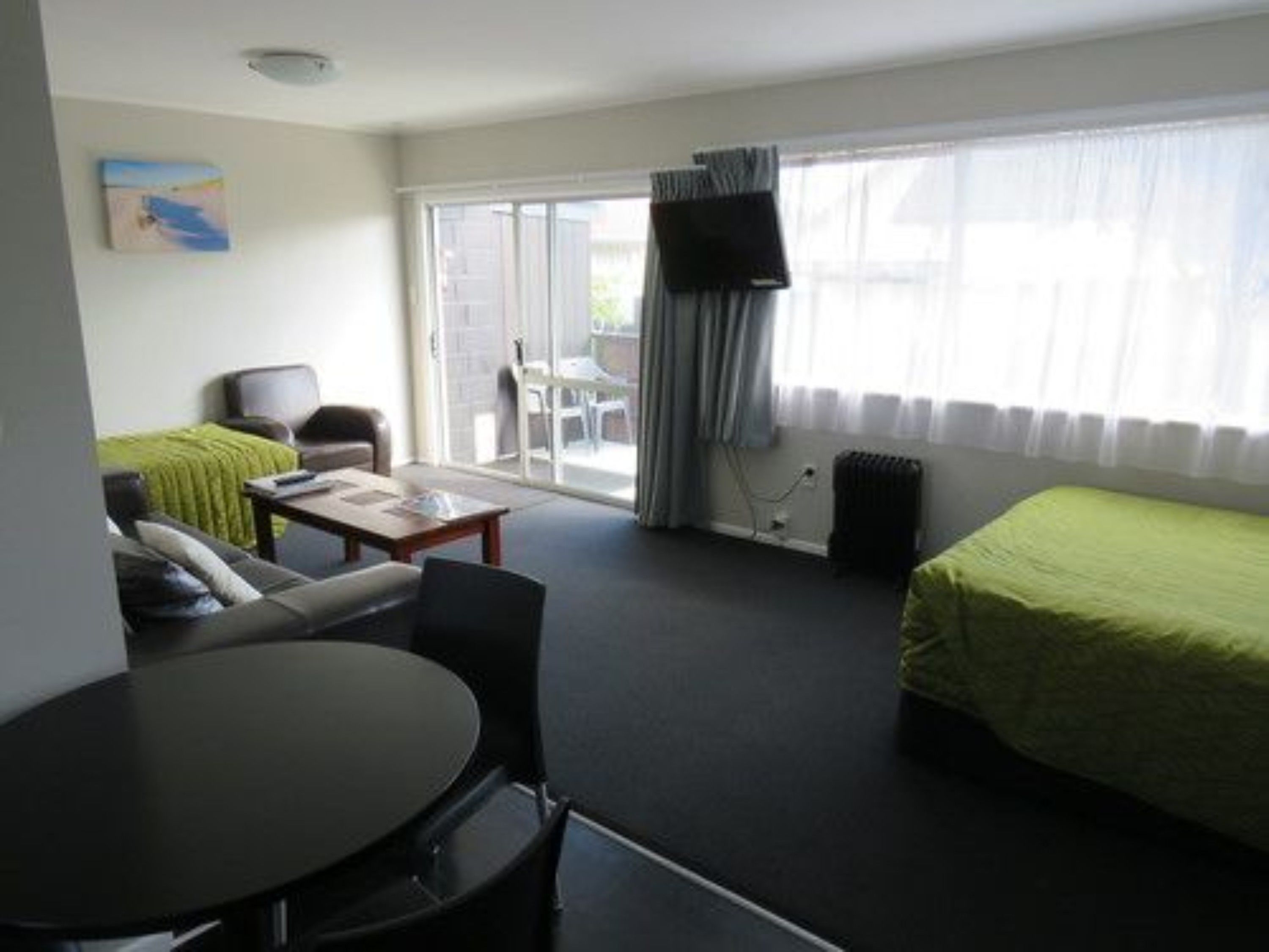 A hotel room with a bed, a desk, a chair, and a sofa. There is a window with curtains and a view of the outside.