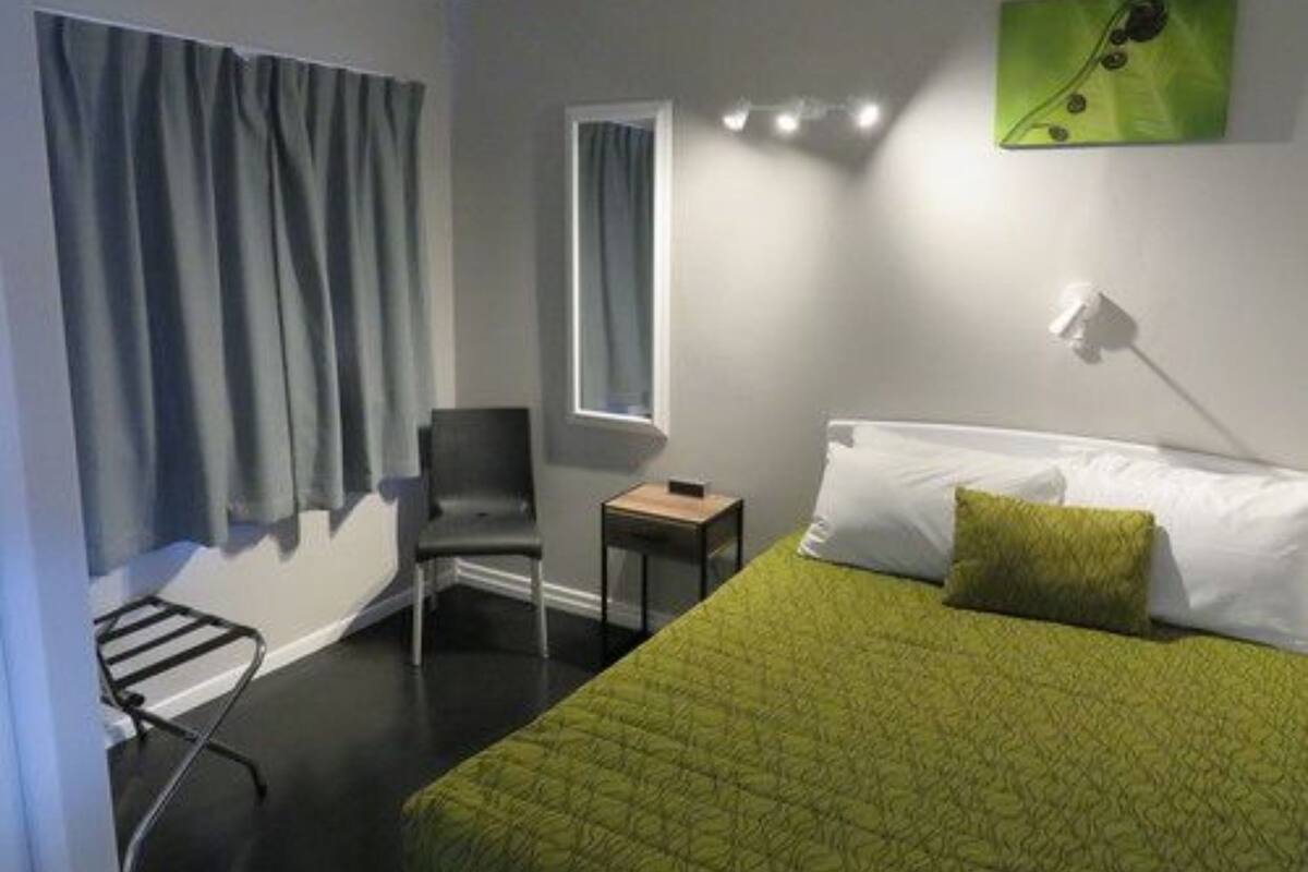 A hotel room with a bed, a chair, a small table, and a window with curtains.