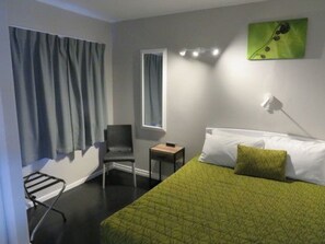 Una habitación de hotel con cama, una silla, una mesita y una ventana con cortinas.