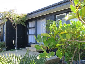 Una casa con fachada oscura, un deck de madera y un pequeño jardín con diversas plantas.