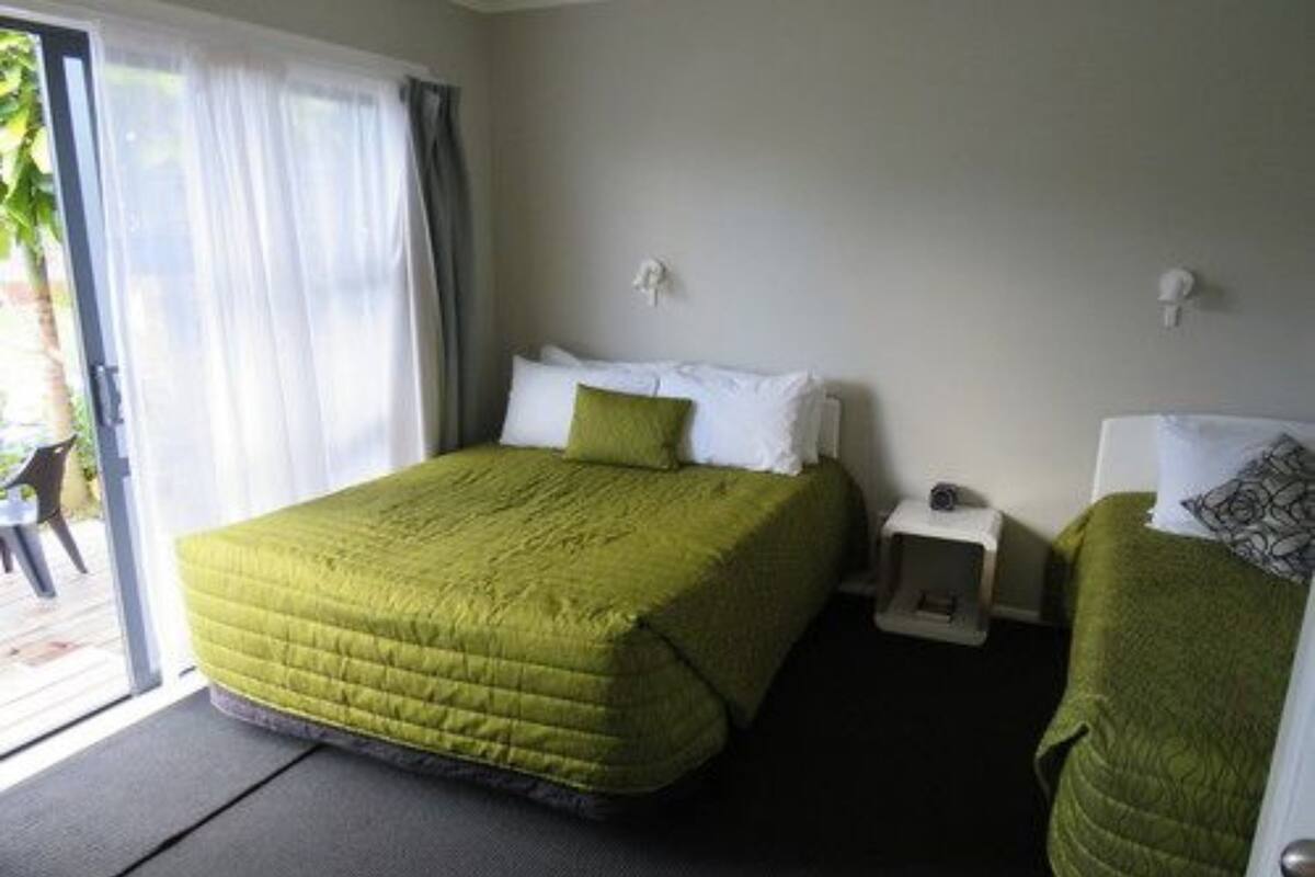 A single-bed room with a green bedspread, white pillows, a small bedside table, and a chair with a green cover.