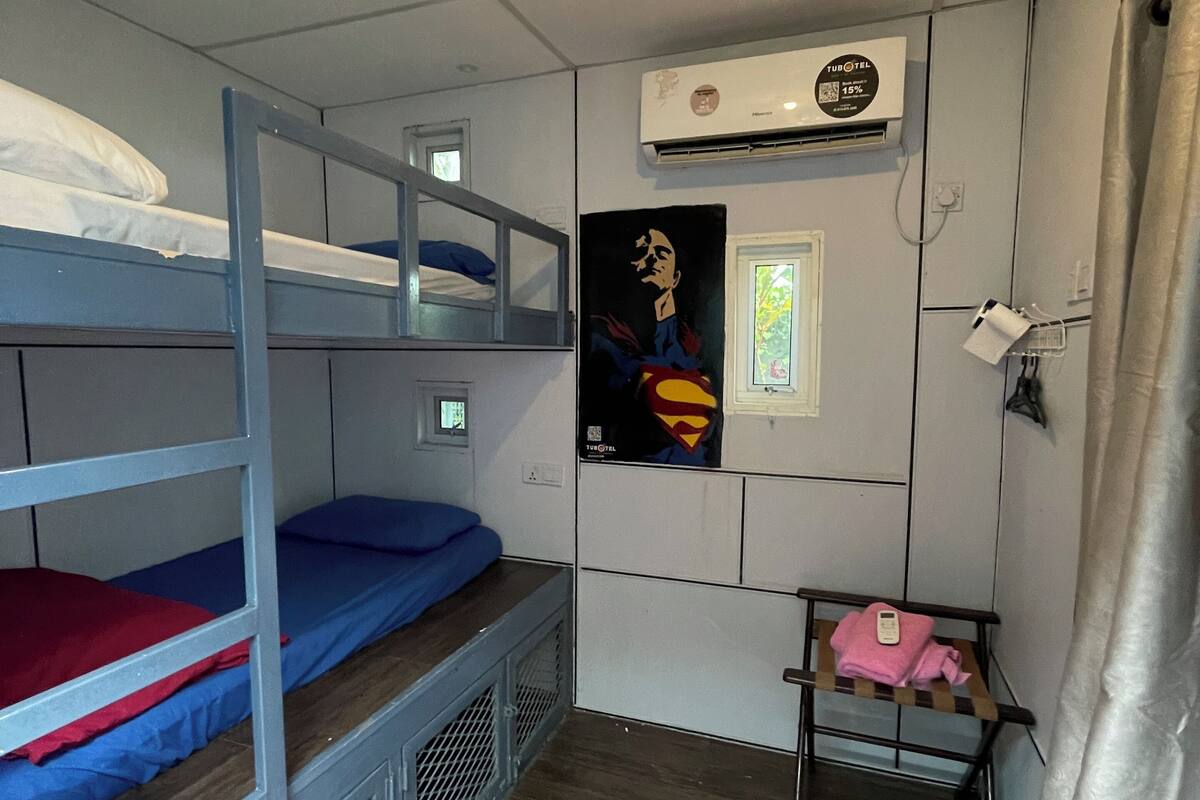 A dormitory room with bunk beds, a poster, an air conditioning unit, and a small table with a towel.