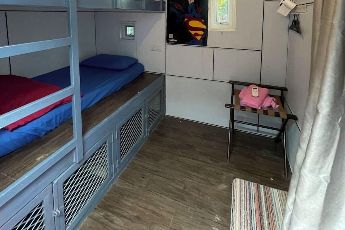A dormitory room with bunk beds, a poster, an air conditioning unit, and a small table with a pink towel.
