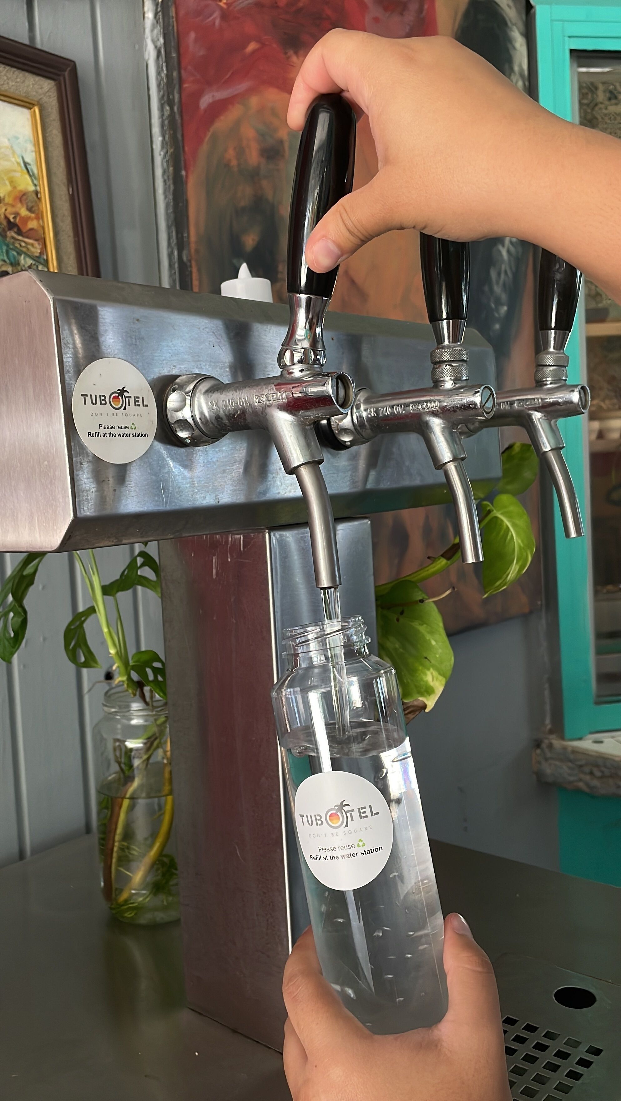 A hand holding a glass jar under a tap with a label that reads "TUBOTEL".
