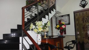 Eine Treppe mit Holzbalken führt zu einer Zwischenebene mit einem Blumenstrauß, einer Uhr und einem gerahmten Bild an der Wand.