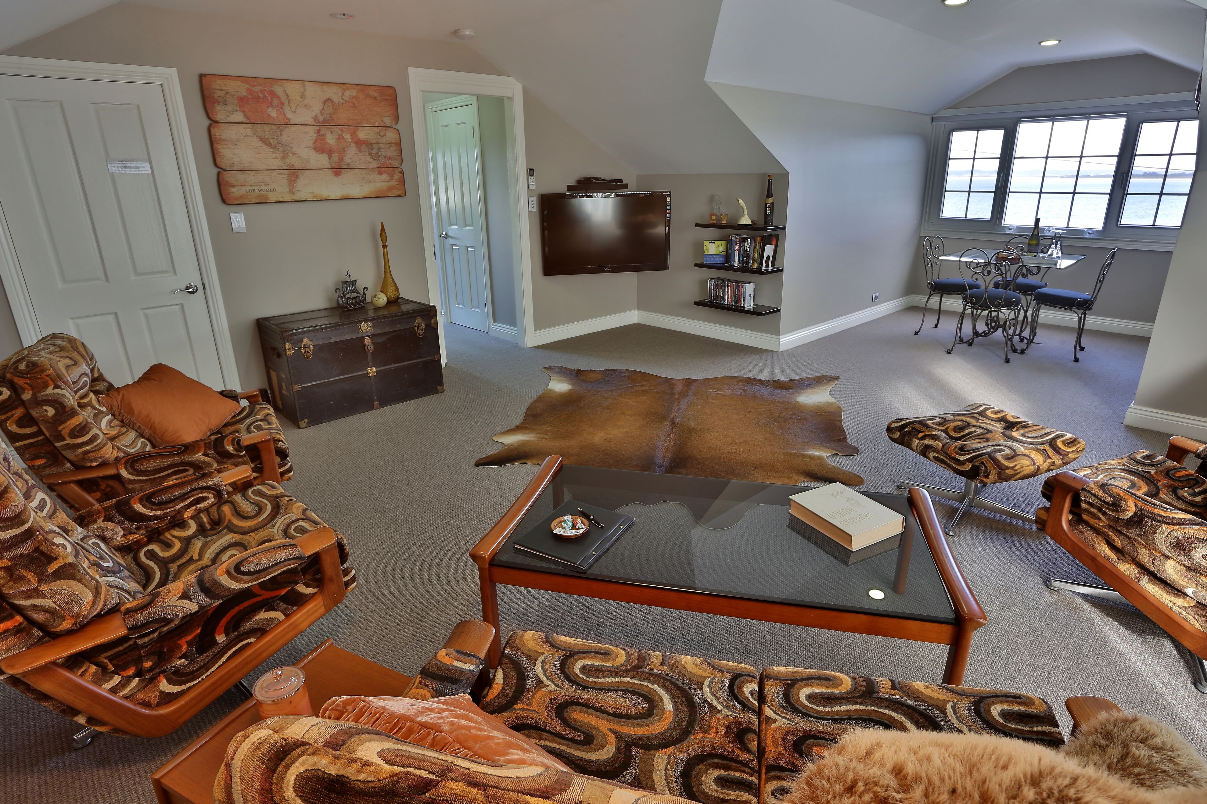 A living room with patterned furniture, a glass-top coffee table, a leather couch, and a view of the outdoors through large windows.