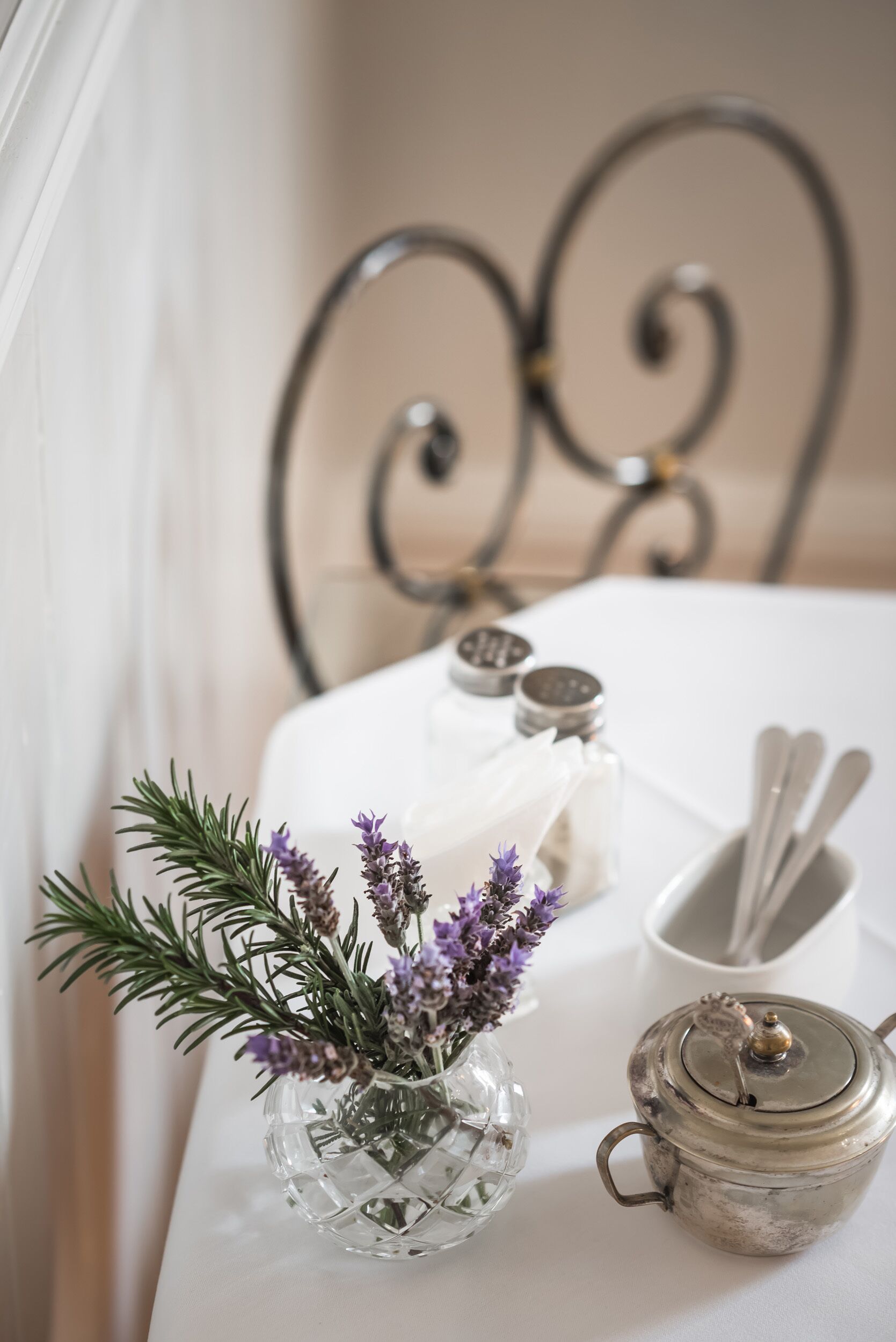 A table with a glass vase of lavender, a salt and pepper shaker set, a white napkin, and a teapot.