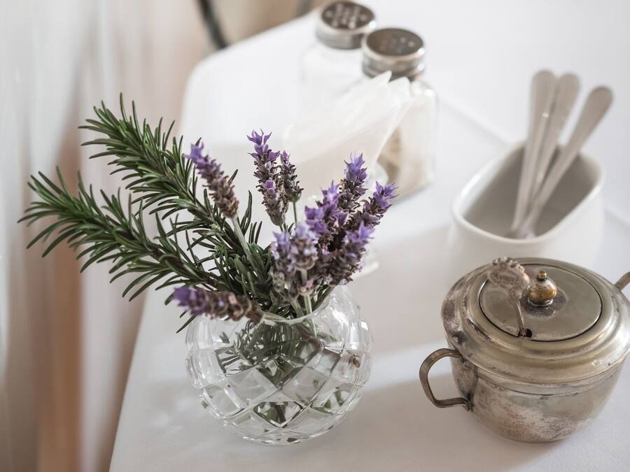 A table with a glass vase of lavender, a salt and pepper shaker set, a white napkin, and a teapot.