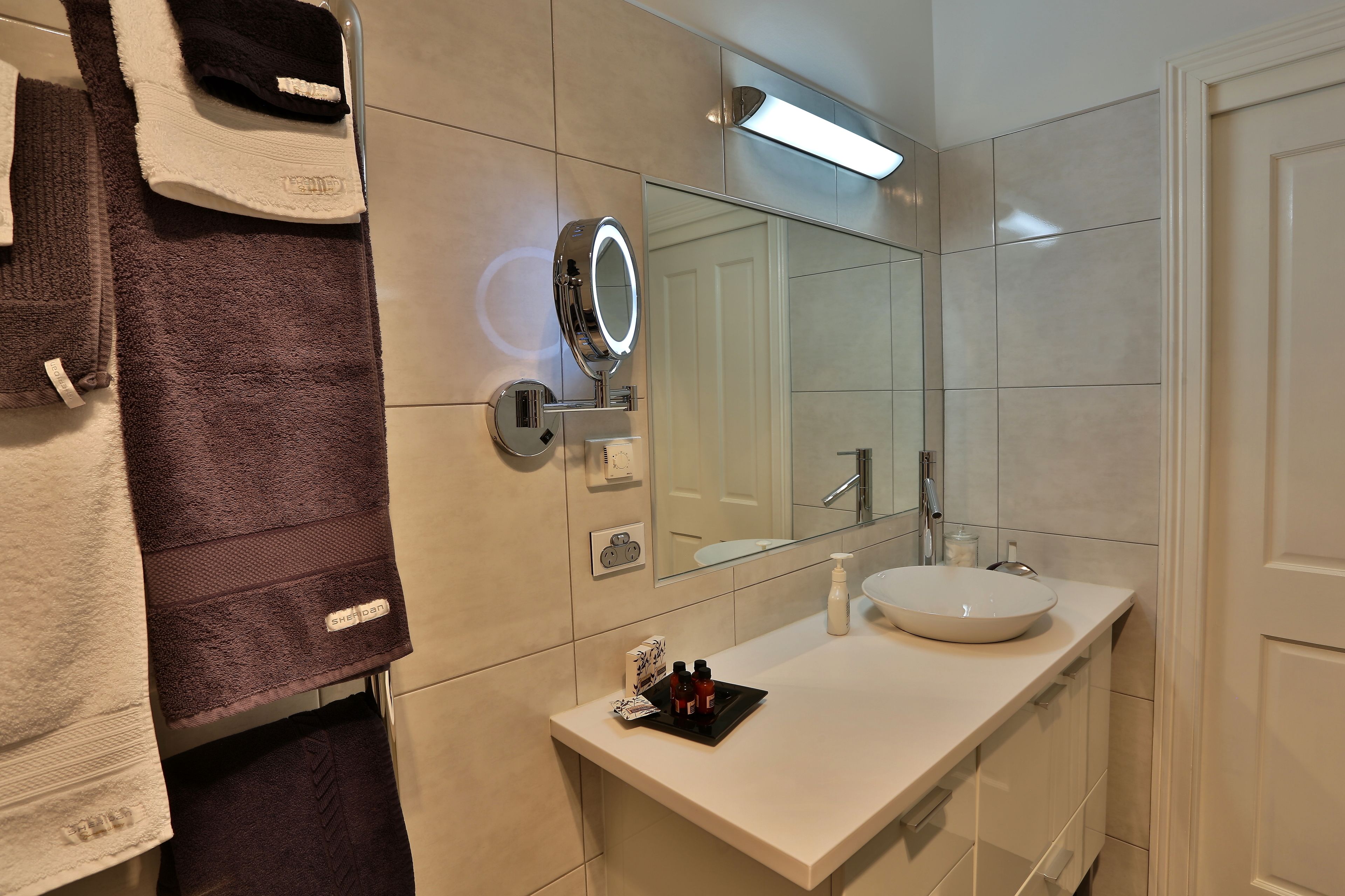 A modern bathroom with a white sink, a mirror with a light, and towels hanging on a rack.