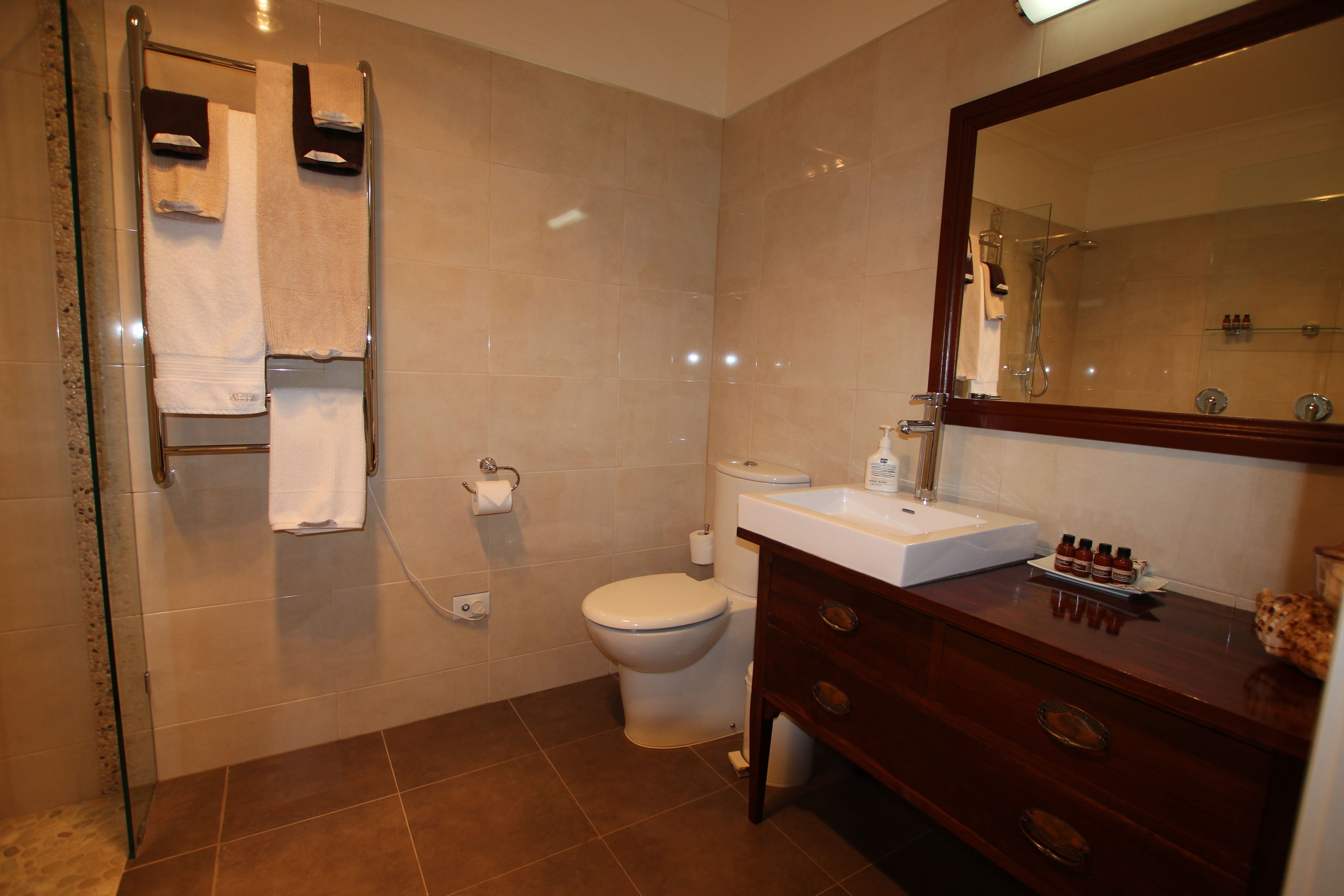 A bathroom with a glass shower enclosure, a white toilet, a sink with a mirror, and a vanity with drawers.
