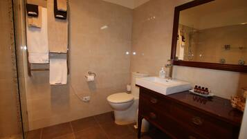 A bathroom with a glass shower enclosure, a white toilet, a sink with a mirror, and a vanity with drawers.