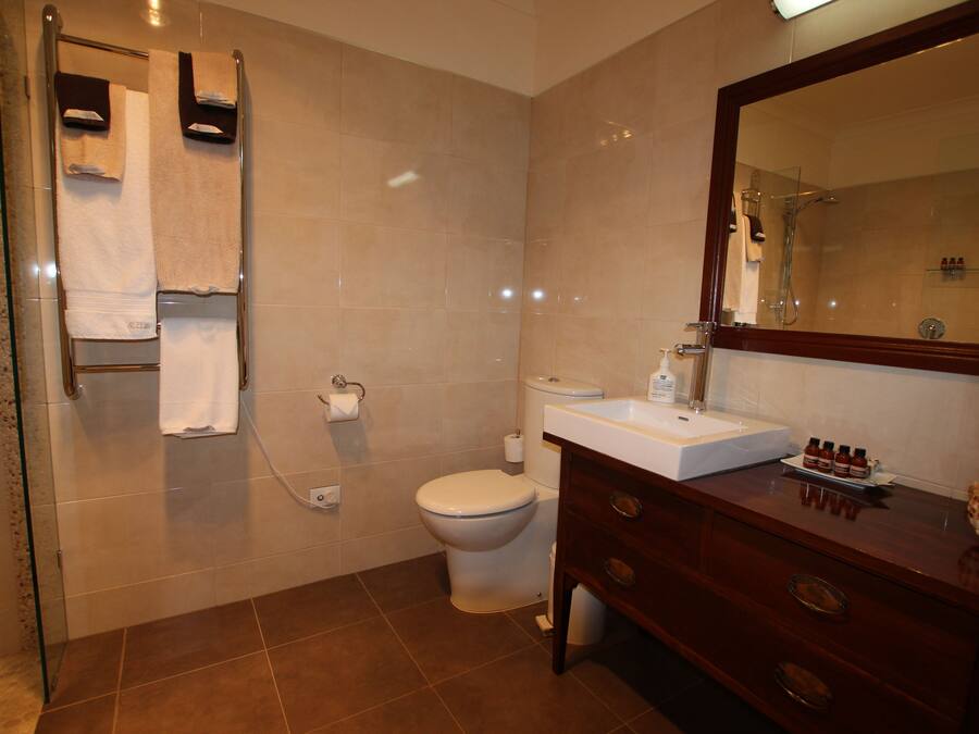 A bathroom with a glass shower enclosure, a white toilet, a sink with a mirror, and a vanity with drawers.