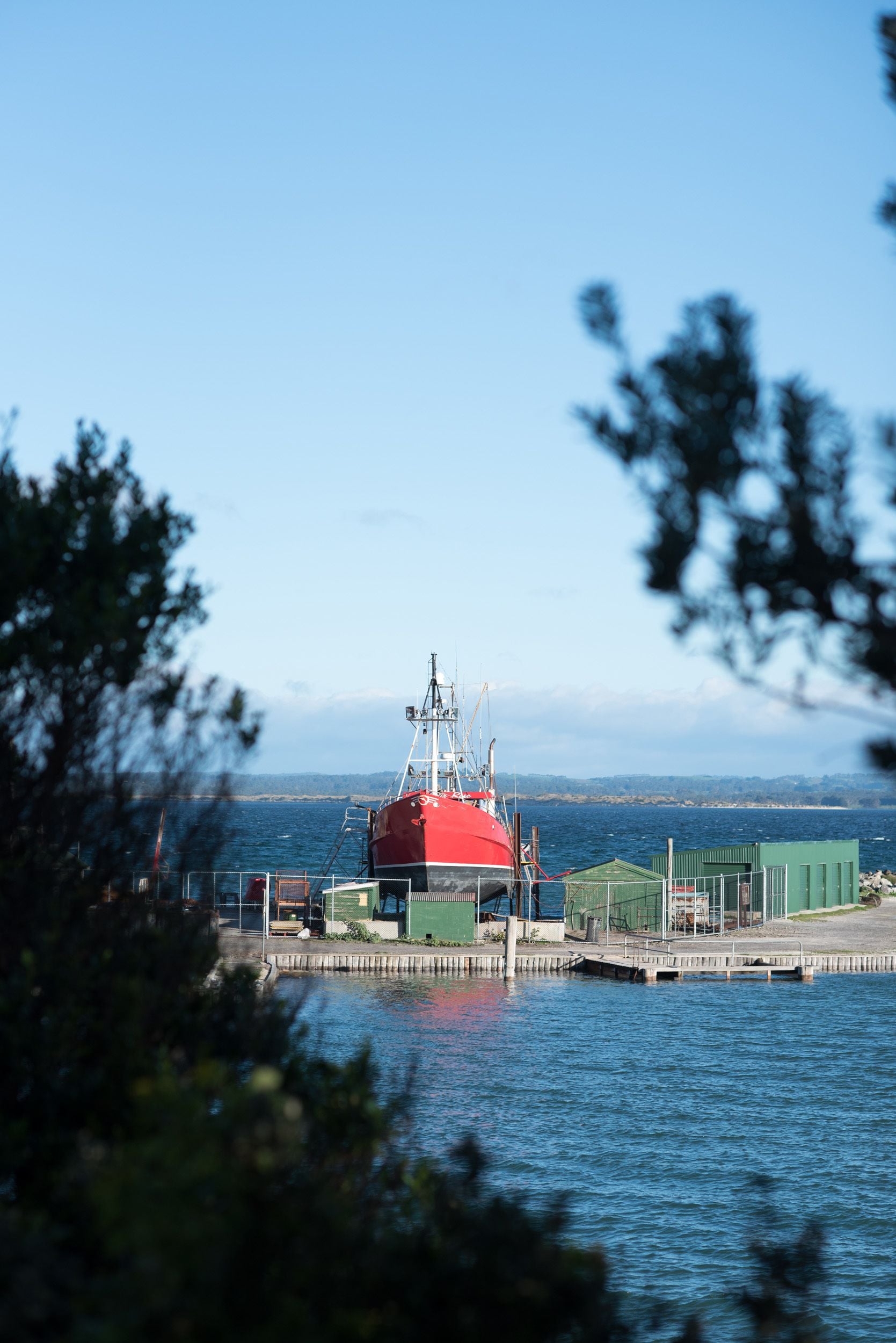 A red cylindrical structure with a crane on a dock by a body of water.
