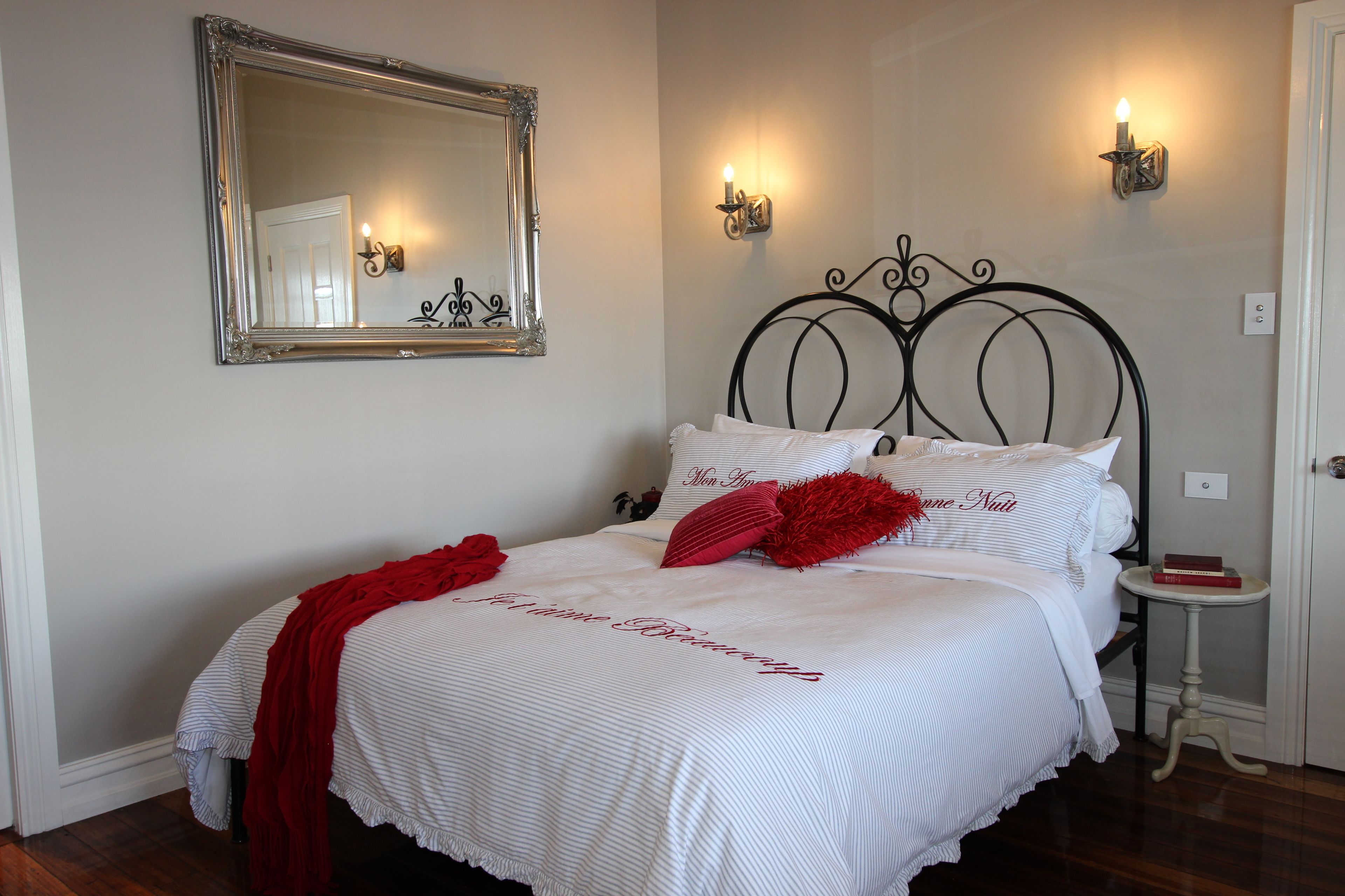 A neatly made bed with a red throw blanket and pillows, a large mirror, and two wall-mounted lights.