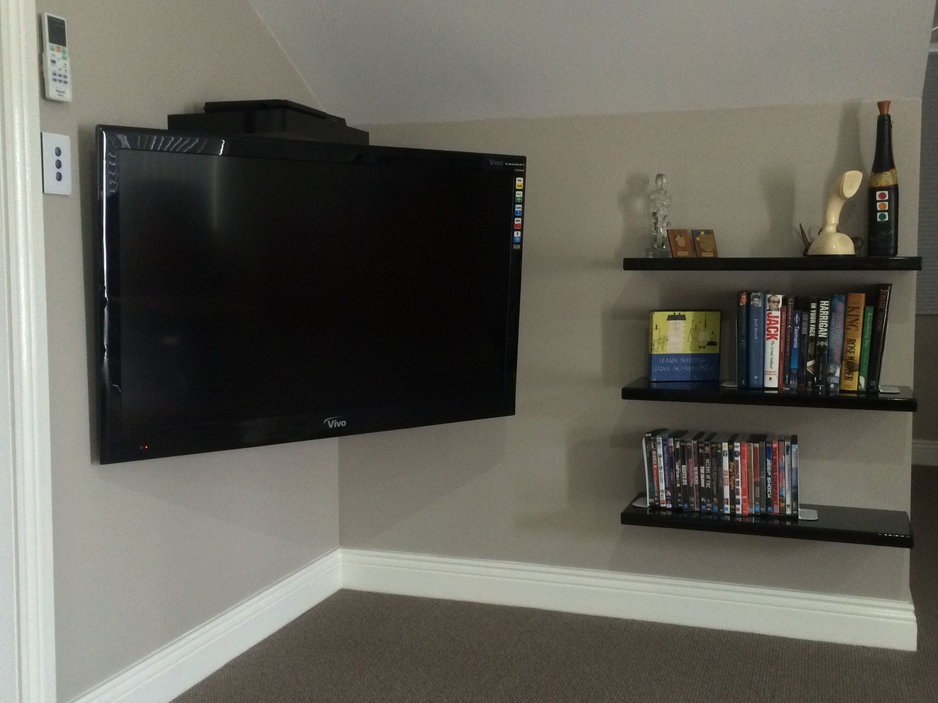 A flat-screen TV mounted on a wall, a bookshelf with books and decorative items, and a thermostat on the wall.