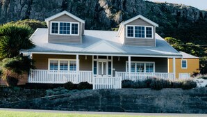 A two-story house with a front porch, a stone retaining wall, and a mountain backdrop. - The Ark Stanley (Stanley)