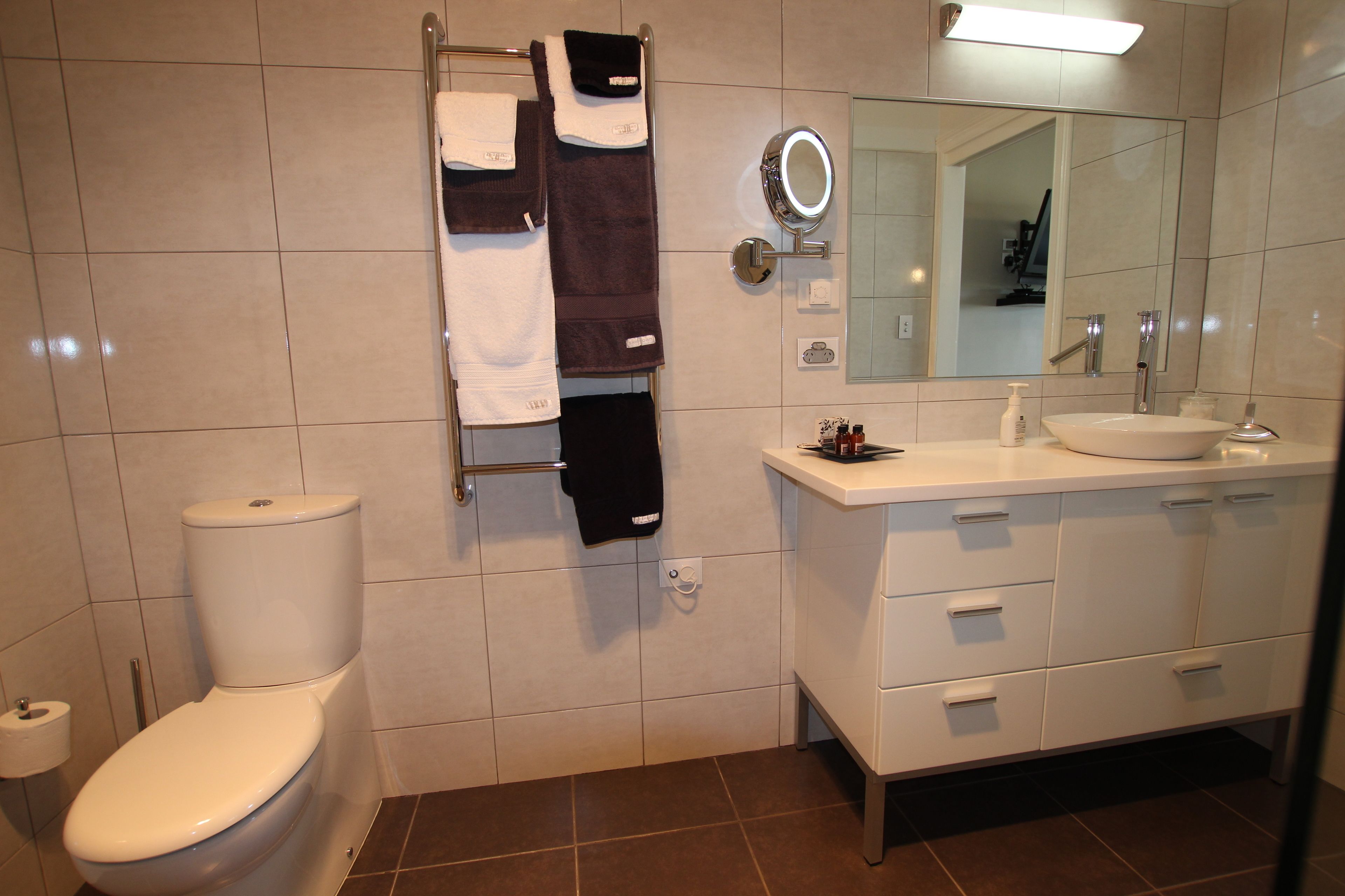 Een moderne badkamer met toilet, een handdoekrek met handdoeken, een wastafel met spiegel en een kast.