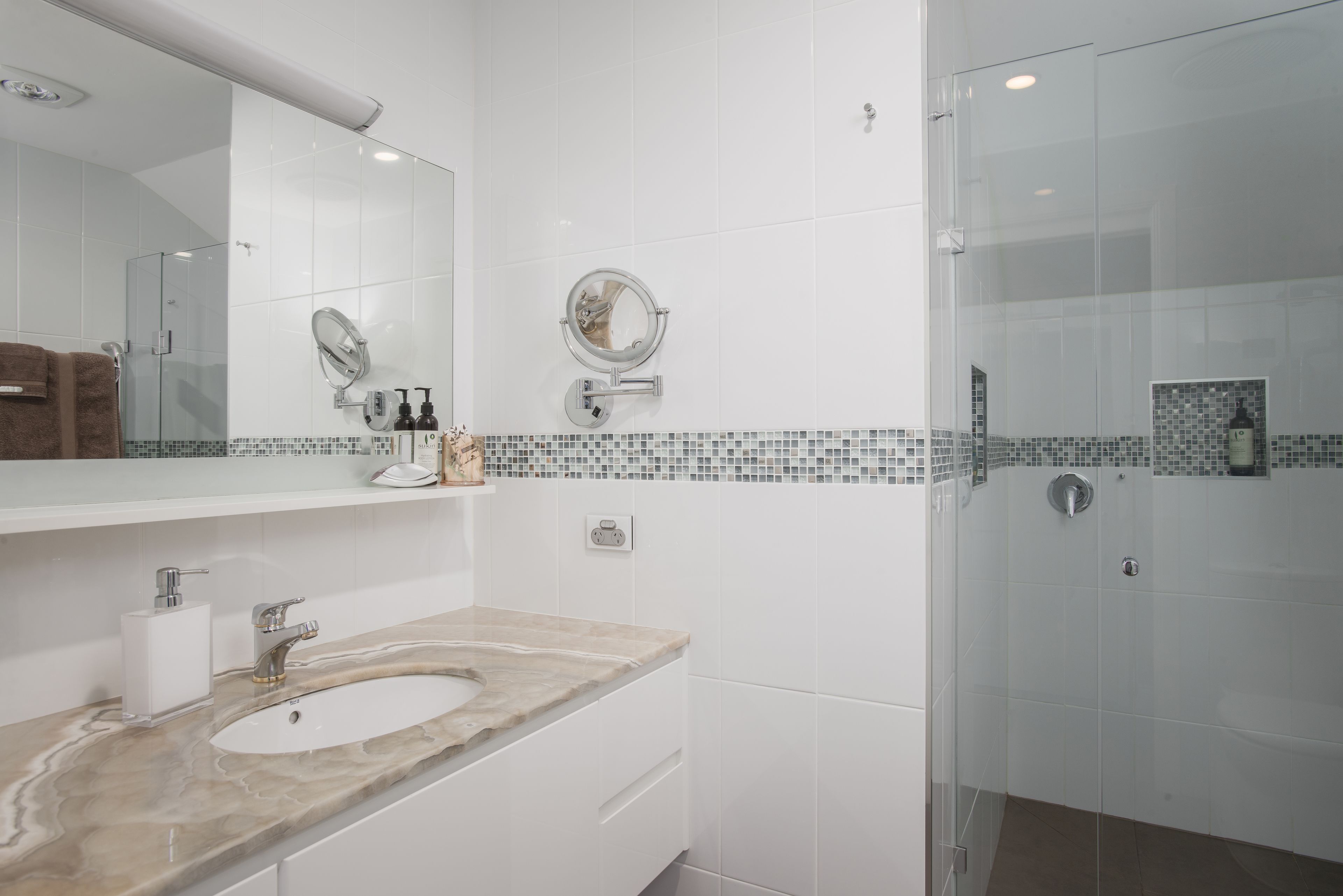 Un baño moderno con lavamanos de mármol, un espejo grande y una mampara de ducha de vidrio.