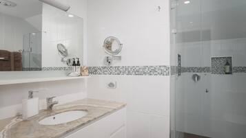 A modern bathroom with a marble sink, a large mirror, and a glass shower enclosure.