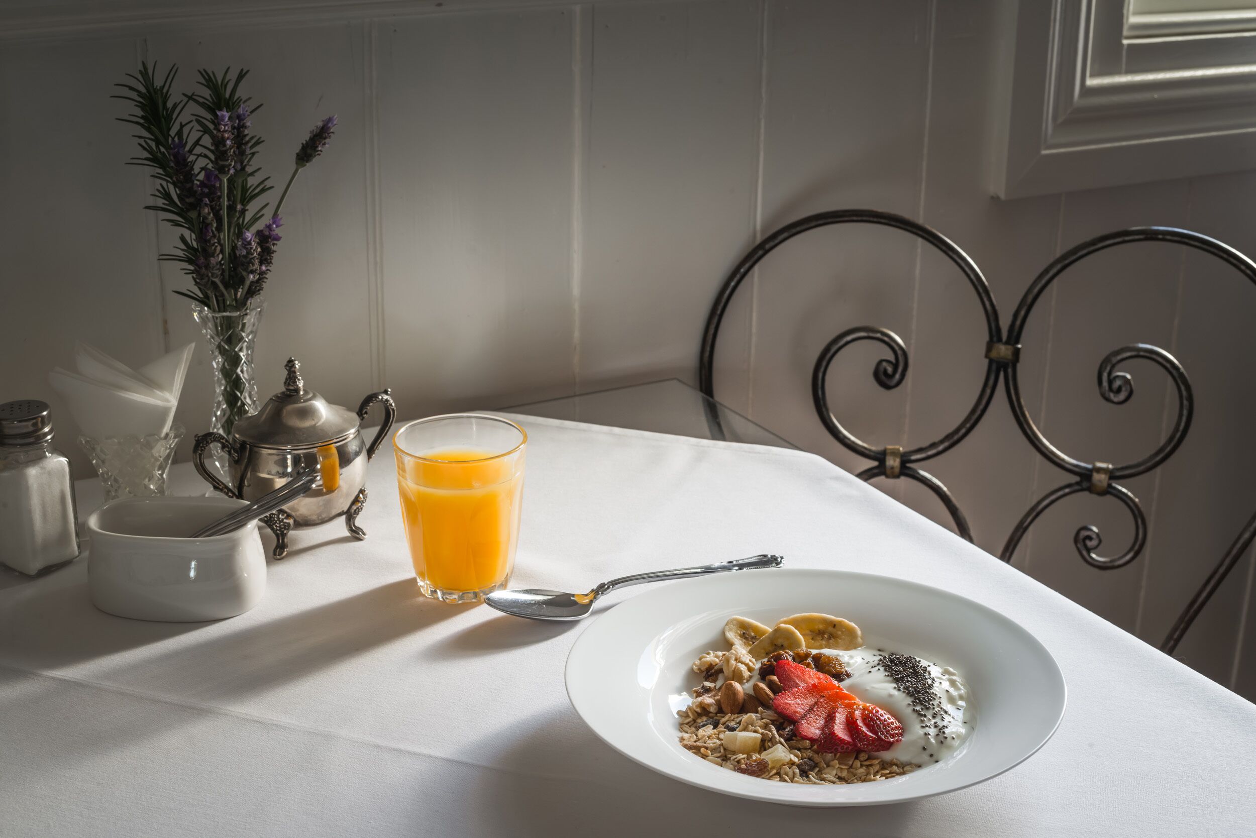 Una mesa de desayuno con un plato de cereal, un vaso de jugo de naranja y un florero con flores.