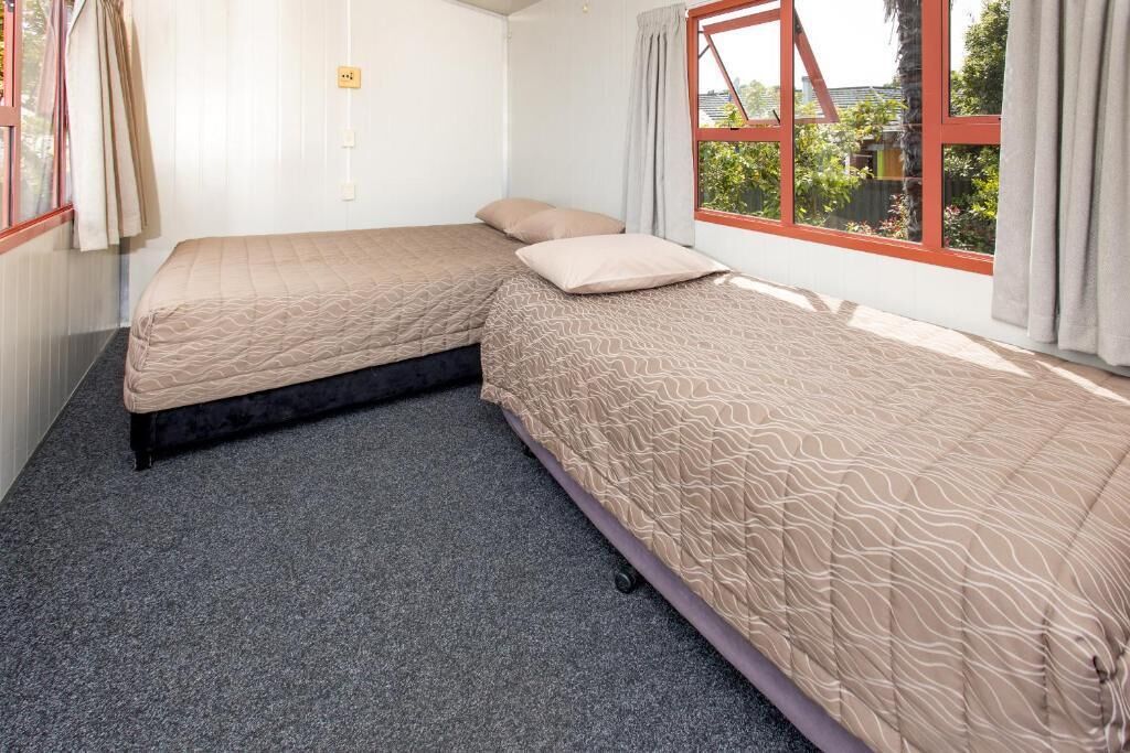 Una habitación con dos camas, un ventanal con vistas a zonas verdes y suelo alfombrado.