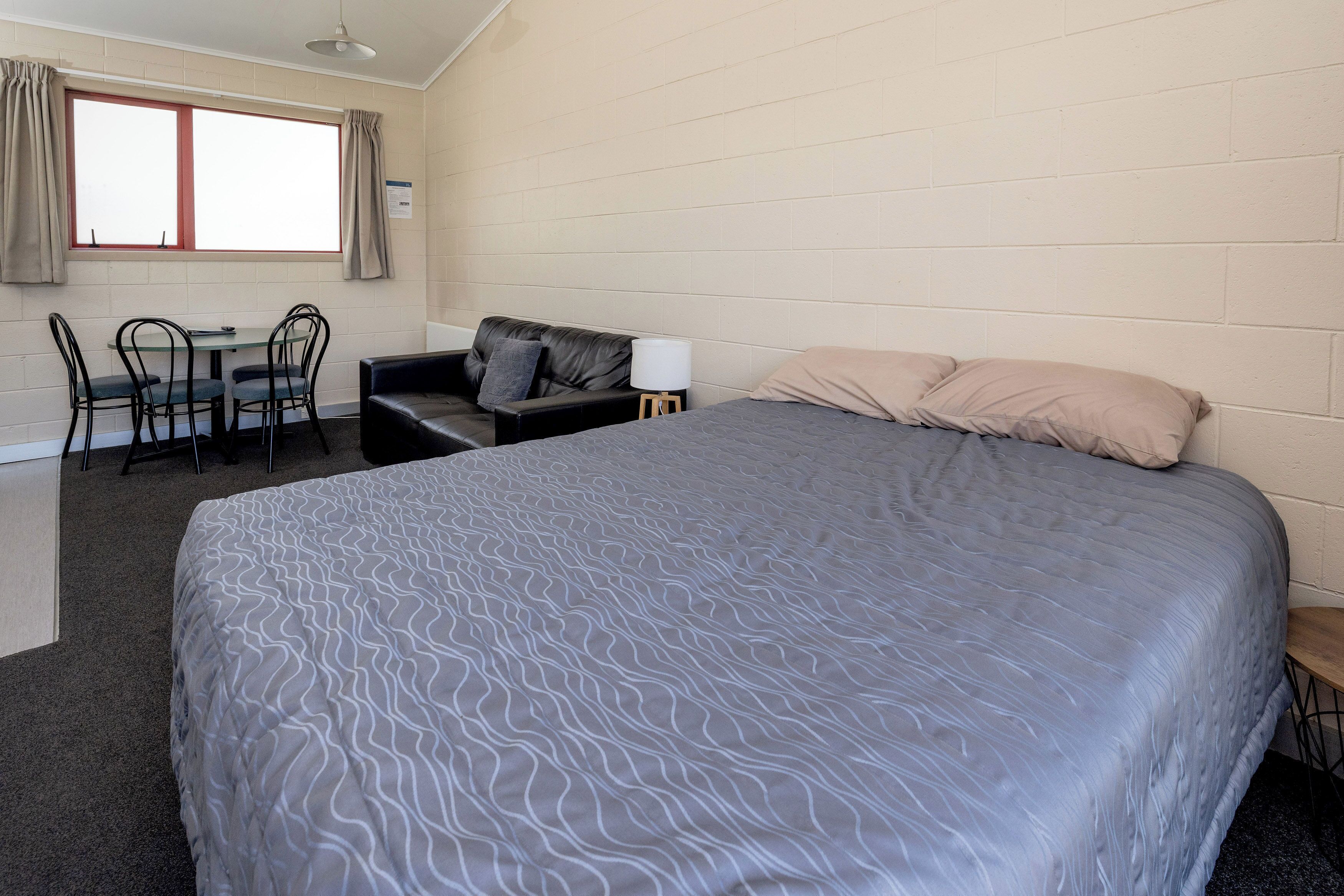 A room with a large bed, a sofa, a table with chairs, and a window with curtains.