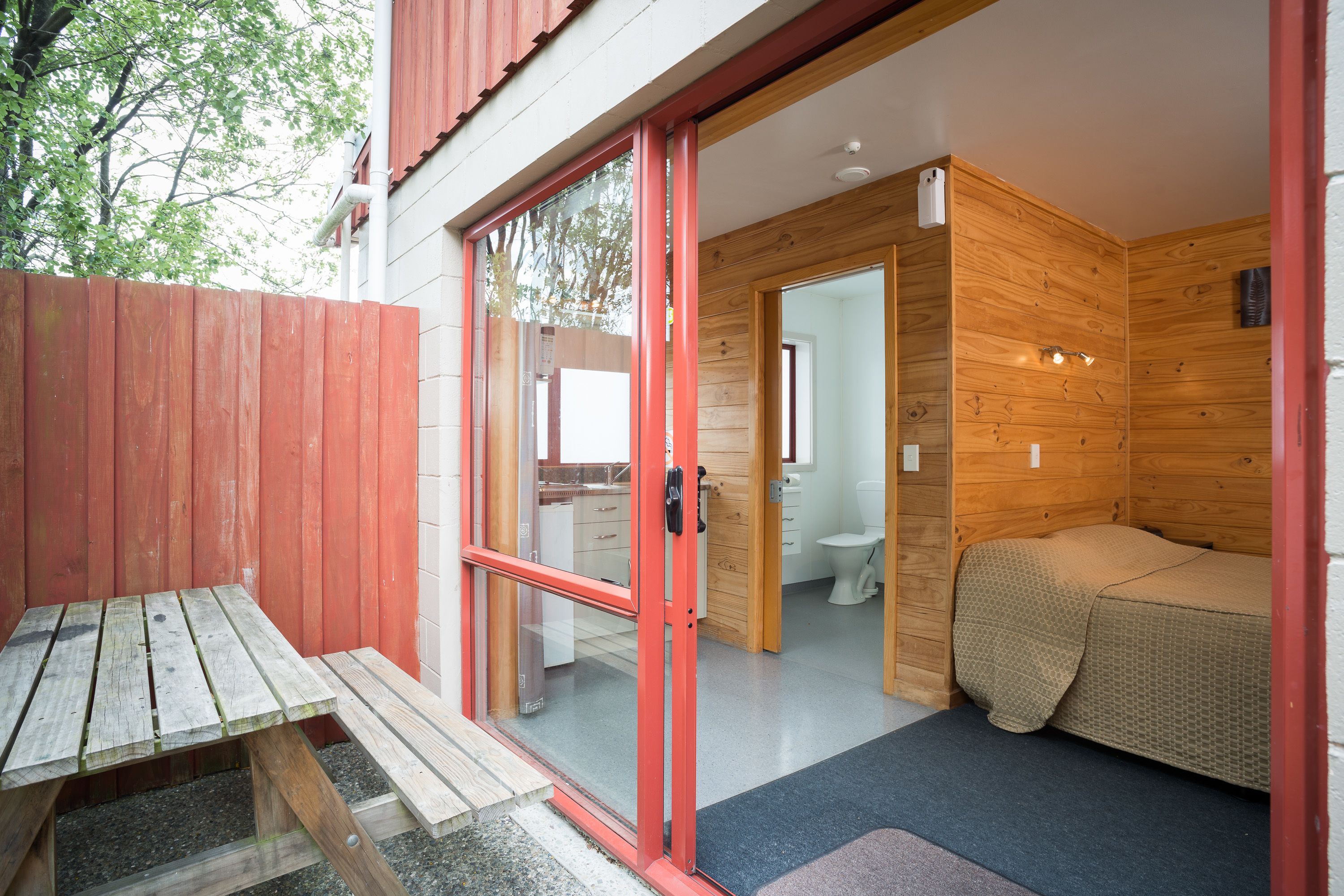 Una cabaña de madera con una puerta corredera de vidrio que da a un baño y un dormitorio pequeño.