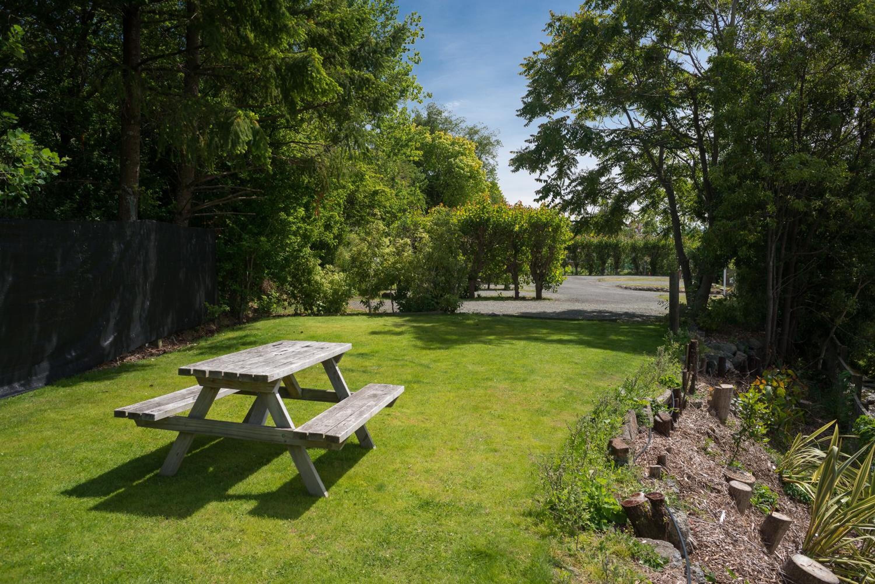 Une table de pique-nique se trouve dans un espace herbeux, avec des arbres et une clôture en arrière-plan.
