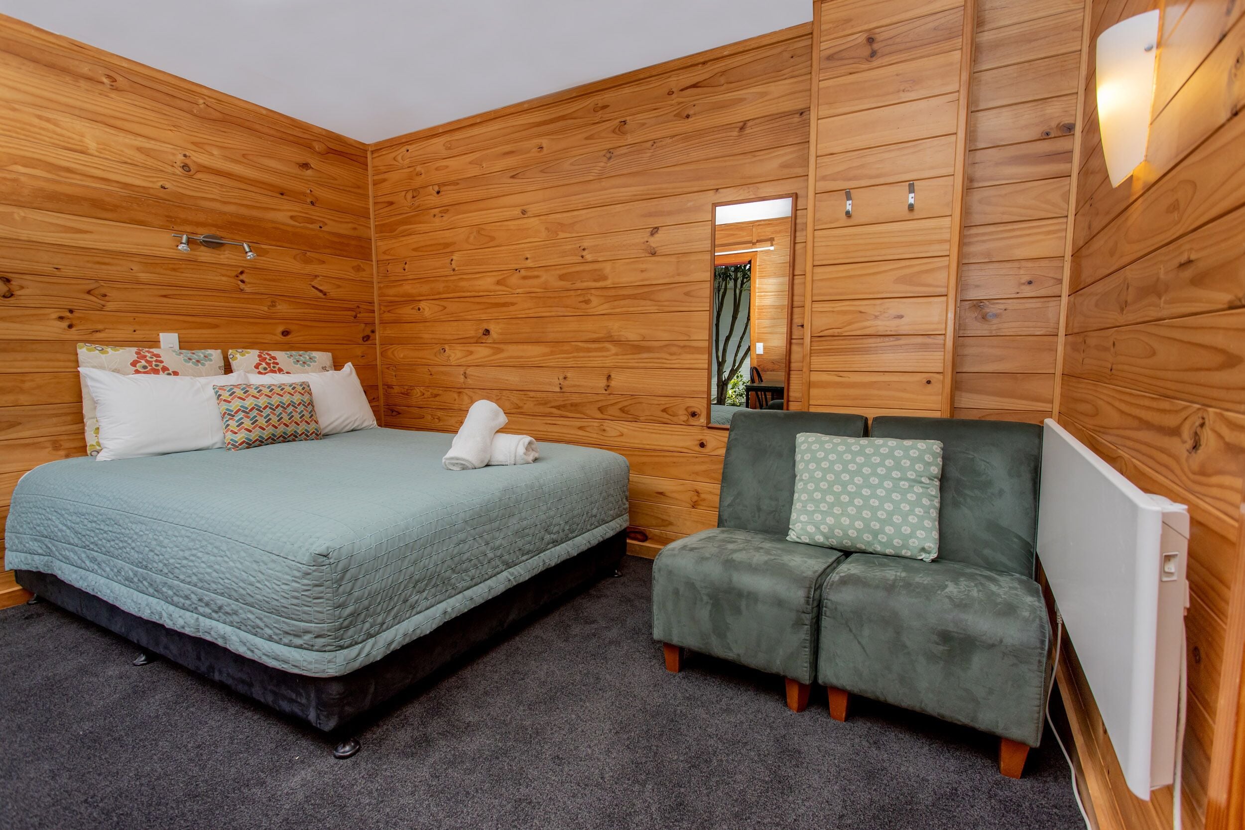 A wooden-paneled room with a bed, a green sofa, and a mirror.
