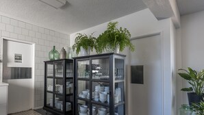 A kitchen with two glass-fronted cabinets on wheels, white tiled walls, and a potted plant on top. - Harriet House Tumut (Tumut)