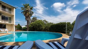 A swimming pool with lounge chairs, a palm tree, and a building in the background. - Harriet House Tumut (Tumut)