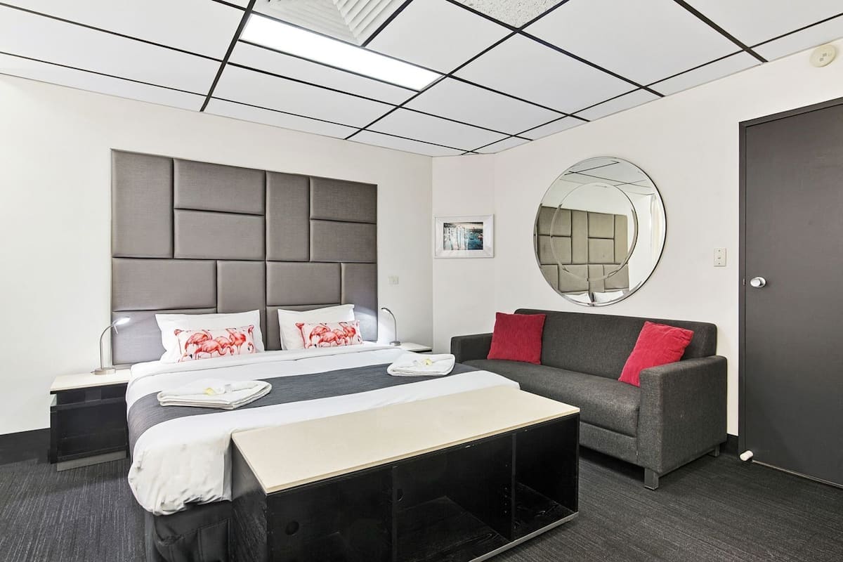 A hotel room with a bed, bedside table, a sofa, a round mirror, and a door.