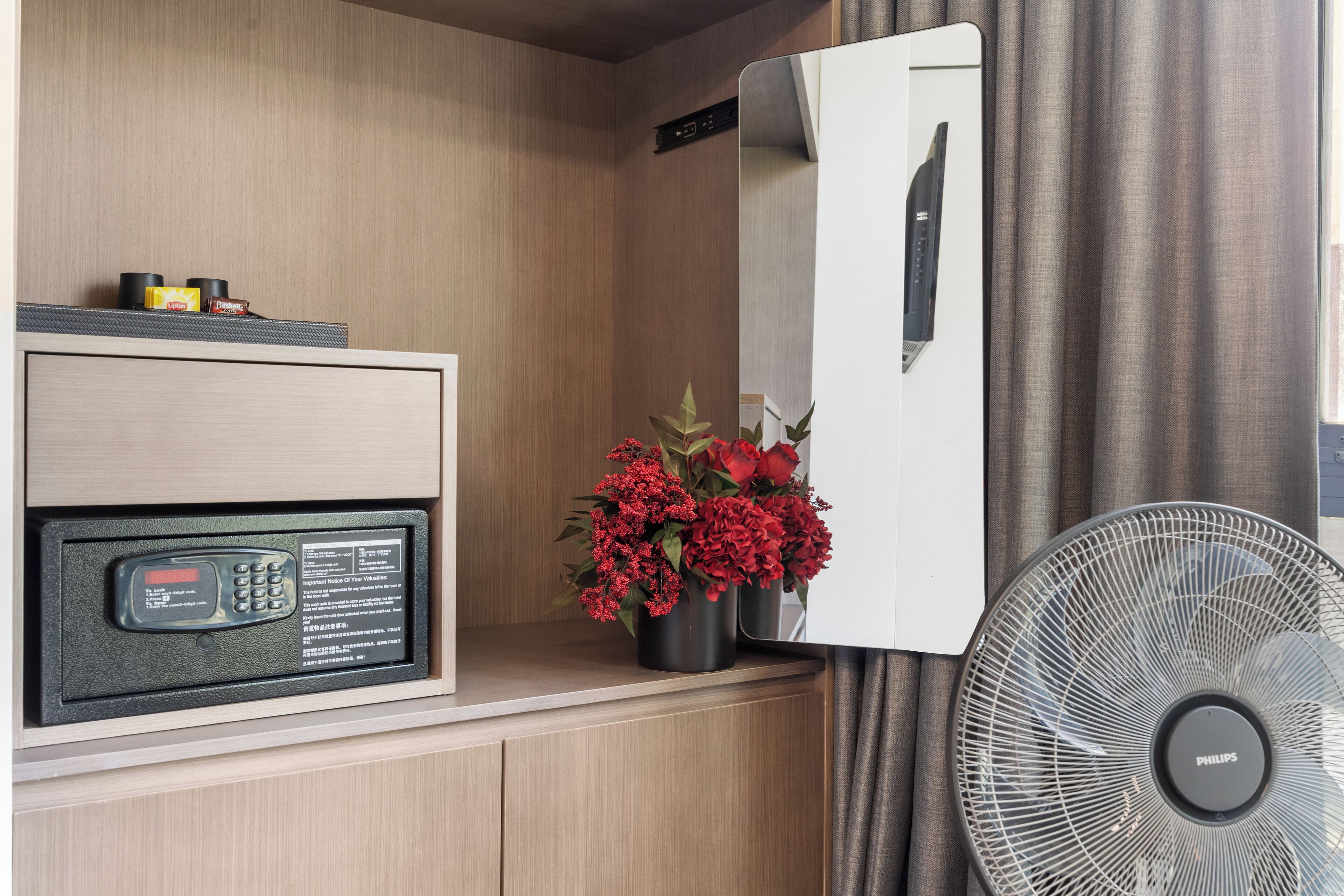 Habitación de hotel con minibar, espejo, ventilador y arreglo floral.