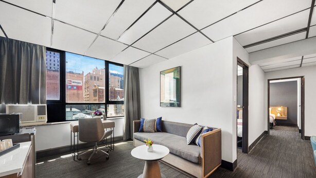 A modern hotel room with a large window, a sofa, a desk, and a small table. - Eminence on Bank (Adelaide)