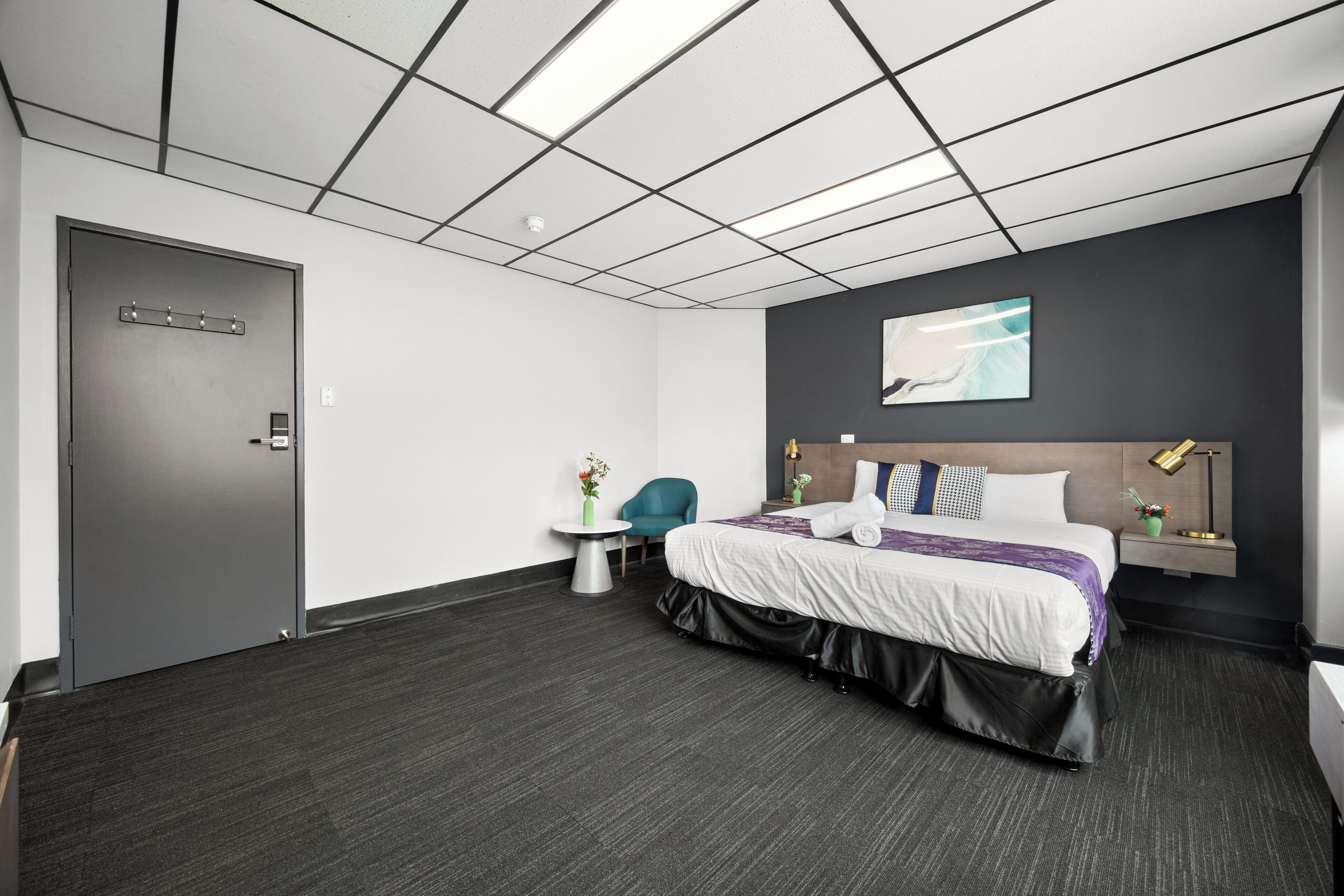 Una habitación de hotel moderna con una cama grande, un escritorio, una silla, una mesita con un jarrón y un cuadro en la pared.