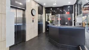 A modern reception area with a marble reception desk, two elevators, and a clock on the wall. - Eminence on Bank (Adelaide)