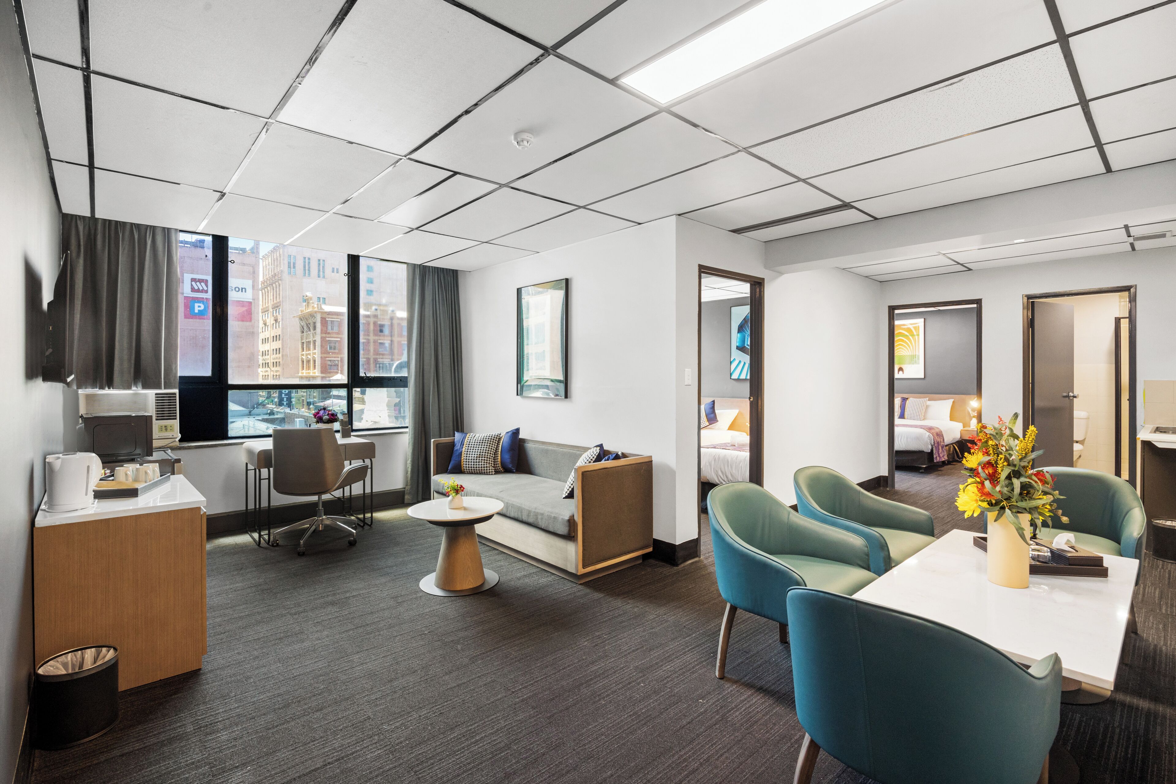 A hotel room with a desk, sofa, chairs, a small table, and a bed.