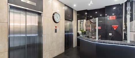A modern elevator area with a clock, a reception desk, and a glass partition.