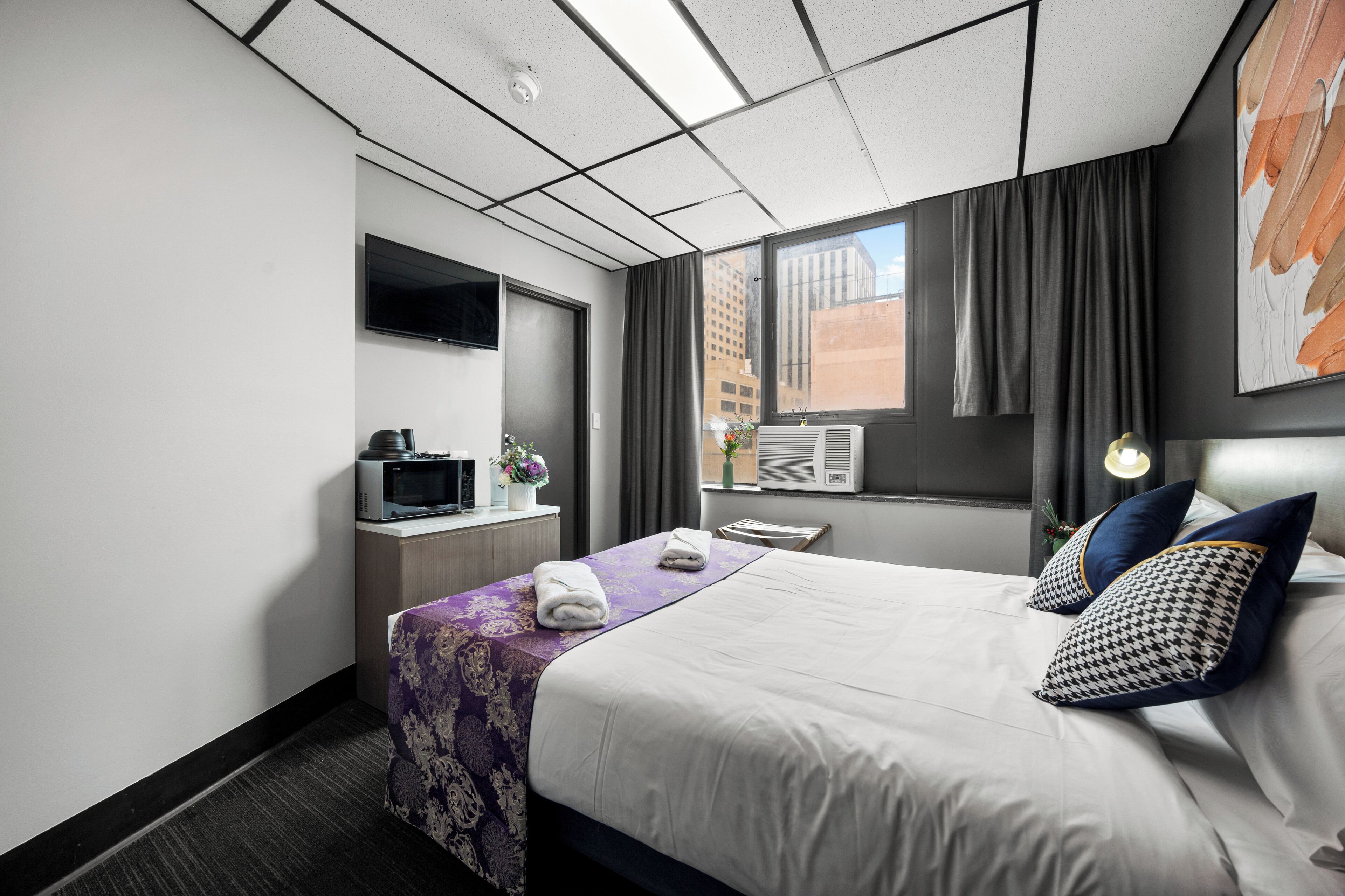 Una habitación de hotel con cama, televisión, escritorio y ventana con cortinas.
