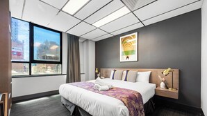 A hotel room with a large bed, a nightstand, a window with a city view, and a painting on the wall. - Eminence on Bank (Adelaide)