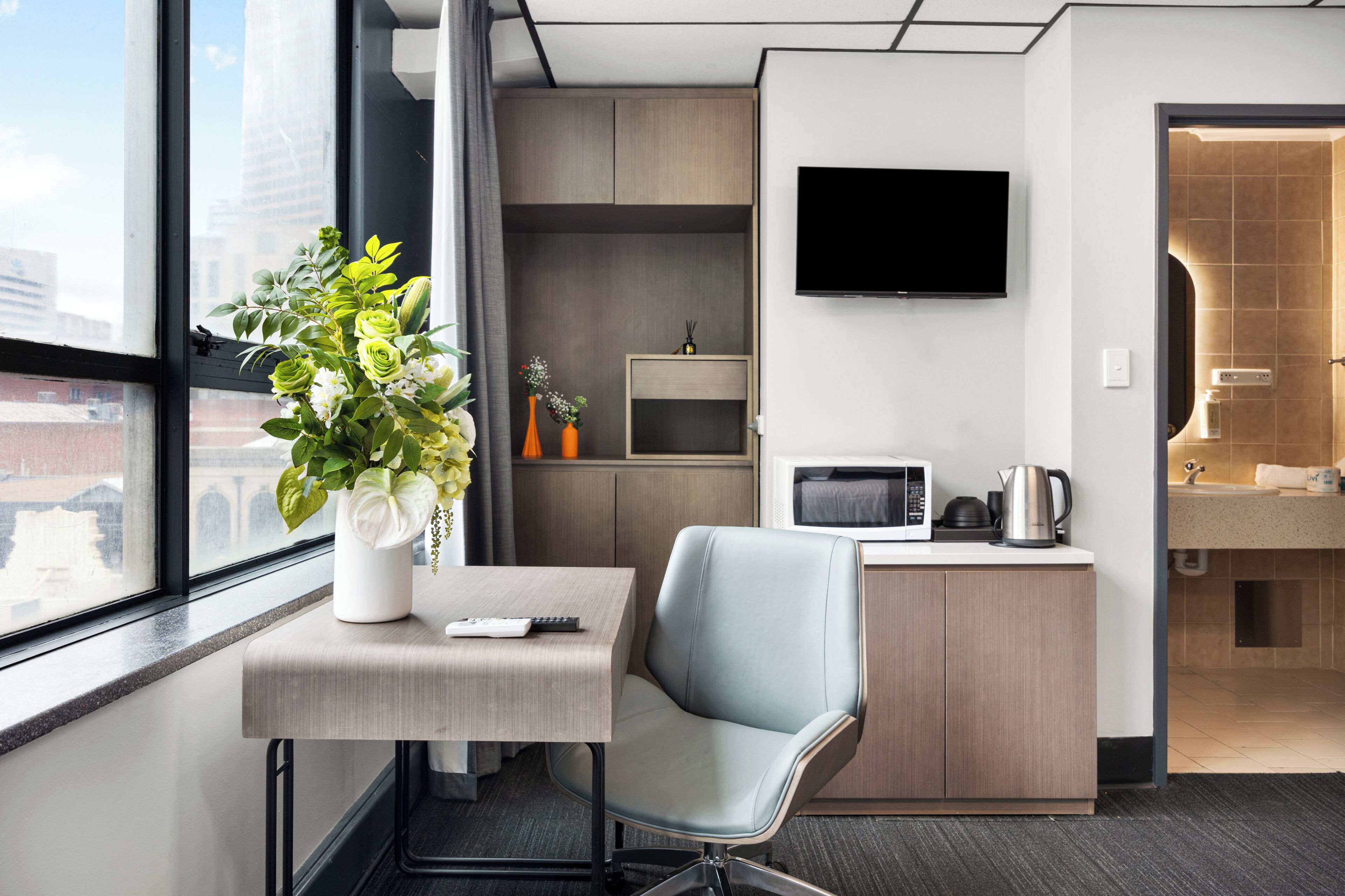 Habitación de hotel con escritorio, silla, televisor, microondas y kitchenette.