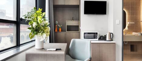A hotel room with a desk, chair, TV, microwave, and kitchenette.