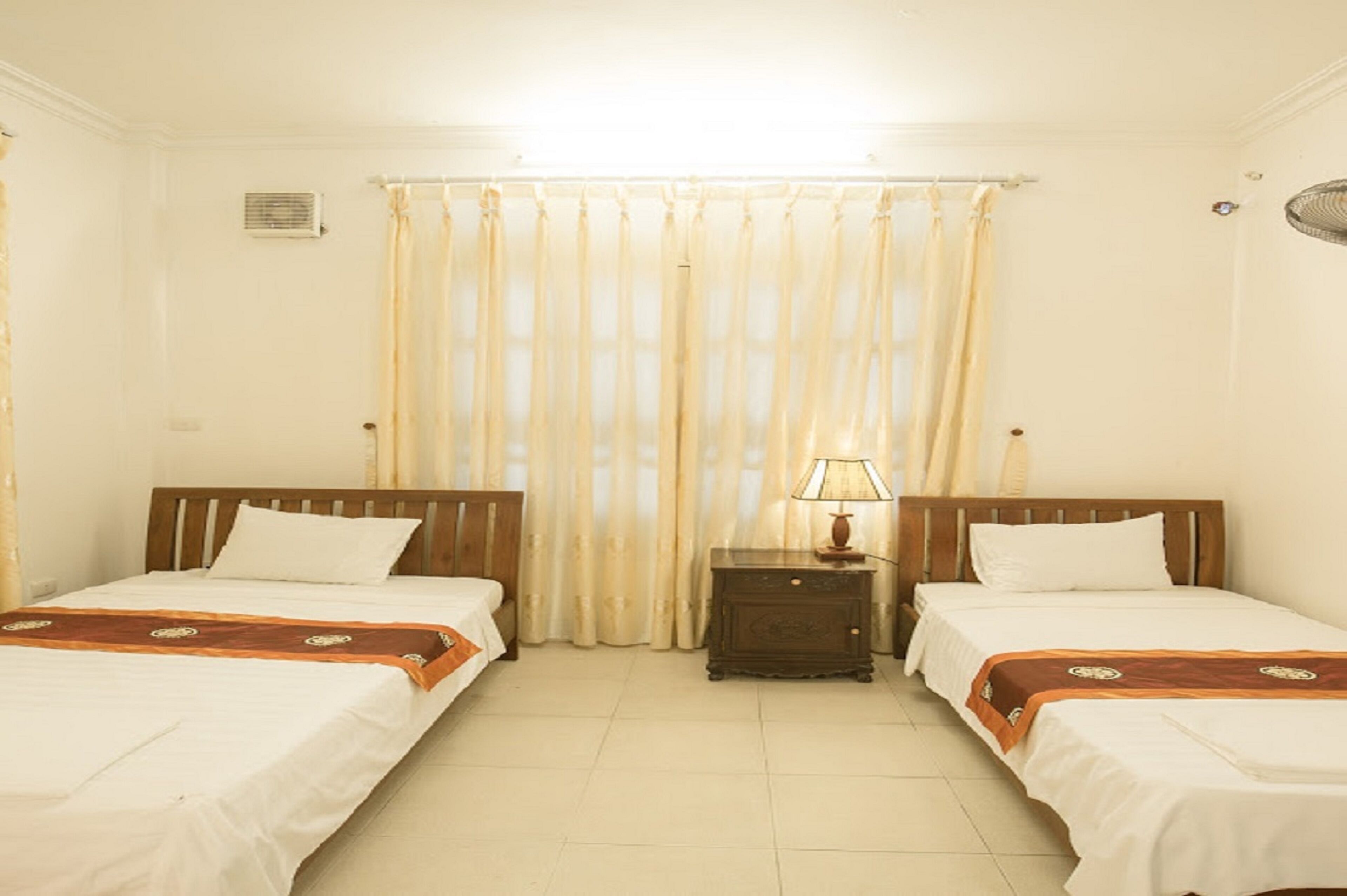 A room with two single beds, a nightstand with a lamp, and a window with curtains.