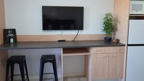 Une cuisine moderne avec un téléviseur à écran plat fixé au mur, des meubles en bois et deux tabourets noirs.