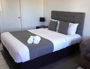 A neatly made bed with a grey and white duvet, two rolled towels, and a grey headboard. - Tumut Apartments (Tumut)