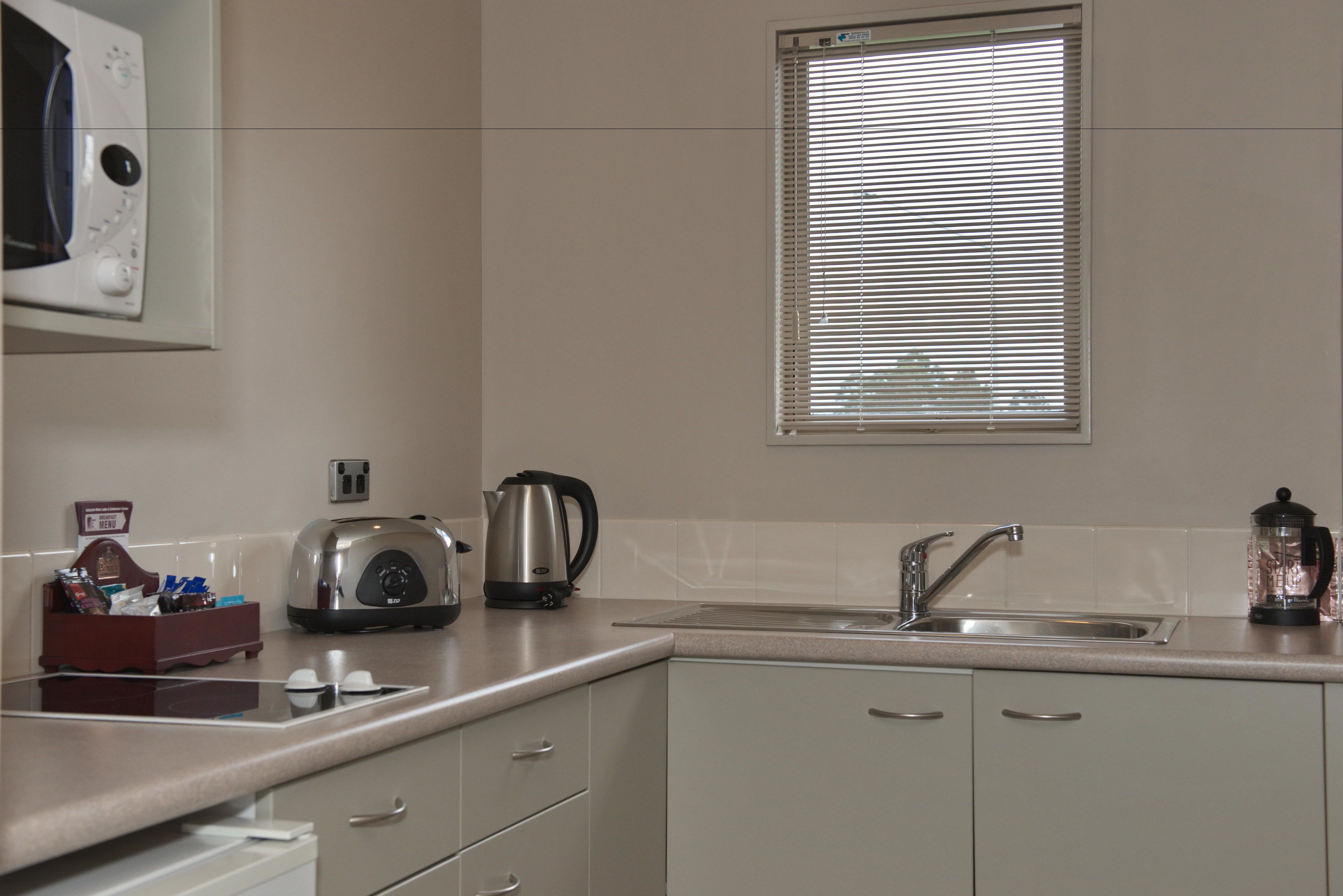 A kitchen with a microwave, toaster, kettle, sink, and a window with blinds.