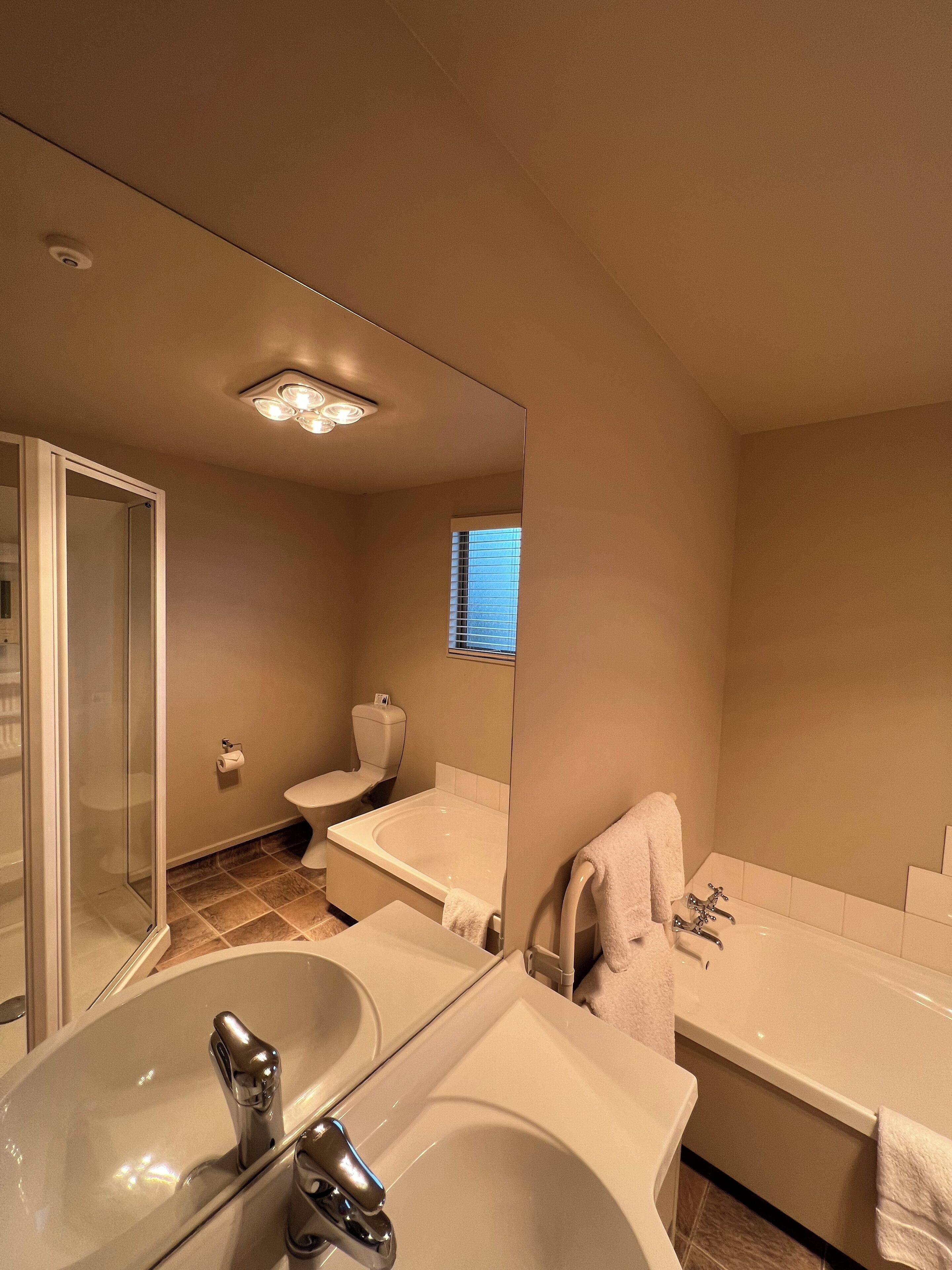 A modern bathroom with a large mirror, a bathtub, a shower area, and a sink.